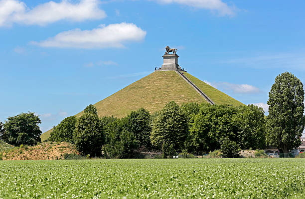 Lion's Mound commemorating the Battle at Waterloo, Belgium. The Lion's Mound (or "Lion's Hillock", "Butte du Lion" in French, "Leeuw van Waterloo" in Dutch) is a large conical artificial hill raised on the battlefield of Waterloo to commemorate the location where William II of the Netherlands (the Prince of Orange) was knocked from his horse by a musket ball to the shoulder during the battle. It was ordered constructed in 1820 by his father, King William I of The Netherlands, and completed in 1826. The prince fought at the preluding Battle of Quatre Bras (16 June, 1815) and the Battle of Waterloo (18 June, 1815). The hill is surmounted by a statue of a lion mounted upon a stone-block pedestal. The model lion was sculpted by Jean-François Van Geel (1756-1830), and bears close resemblance to the 16th century Medici lions. The lion is the heraldic beast on the personal coat of arms of the monarch of The Netherlands, and symbolizes courage; its right front paw is upon a sphere, signifying global victory. The Battle of Waterloo was fought on Sunday, 18 June 1815, near Waterloo in present-day Belgium, then part of the United Kingdom of the Netherlands. A French army under the command of Napoleon was defeated by the armies of the Seventh Coalition, comprising an Anglo-allied army under the command of the Duke of Wellington combined with a Prussian army under the command of Gebhard von Blucher. burial mound photos stock pictures, royalty-free photos & images