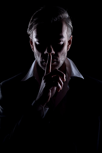 Men's silhouette in the dark shows silence gesture