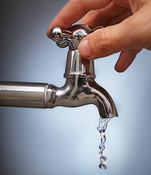 Hand turning silver tap with water dripping out man's hand closes the leakage of water from the faucet Metal faucet leaking pipe water stock pictures, royalty-free photos & images