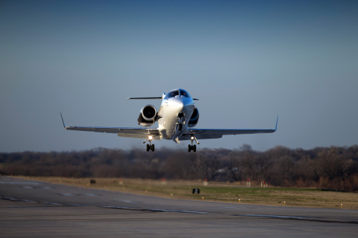 Sleek new business jet climbs away from the runway. Dusk lighting and compressed telephoto perspective emphasizes the aerodynamic fuselage and powerful engines. Pilot's faces are unrecognizable.