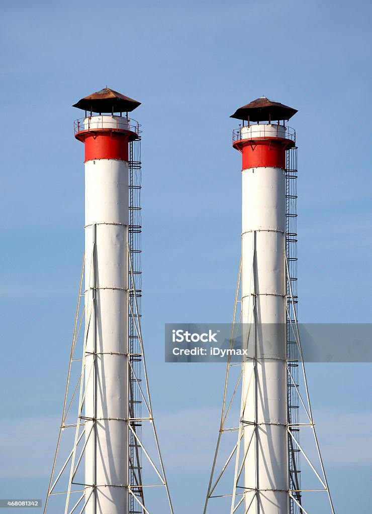 Industrial smoke pipes over blue sky vertical view Two high industrial smoke pipes over clear blue sky vertical view close up 2015 Stock Photo