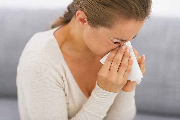 istock young woman sitting on couch and blowing nose 468094667