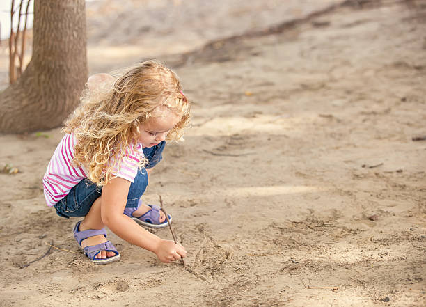 istock Young Girl Drawing With Stick in Sand 468111708