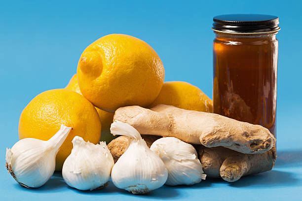 Alternative medicine ingredients of raw honey, whole lemons, ginger root and garlic bulbs on blue.