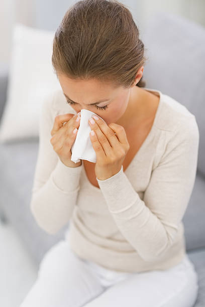 istock young woman sitting on couch and blowing nose 468125523