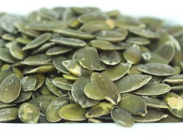 Close-up photo showing some high-protein pumpkin seeds in a small square white dish.  Dried pumpkin seeds are considered to be a 'superfood' with nut-like qualities, since they contain Omega-3 fats and a long list of vitamins, minerals and health benefits.  These include magnesium (for healthy hearts), and zinc (for strong immune systems).