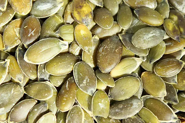 Close-up photo showing some high-protein pumpkin seeds, which are grouped together in a large pile.  Dried pumpkin seeds are something of a 'superfood' in the nut world, since they contain Omega-3 fats and a long list of vitamins, minerals and health benefits.  These include magnesium (for healthy hearts), and zinc (for strong immune systems).