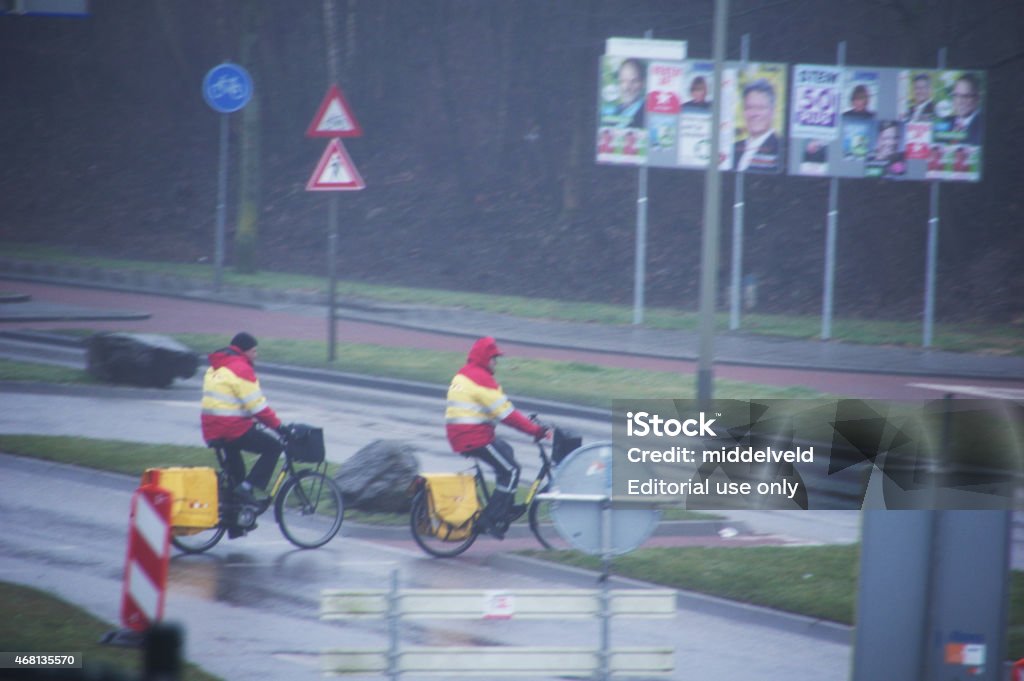 Two postman on there bicycle Brunssum, the Netherlands - March 10, 2015 : Two biking postman crossing the road for serving the morning post. As you can see it is raining but they do there job in all weather conditioning's. 2015 Stock Photo