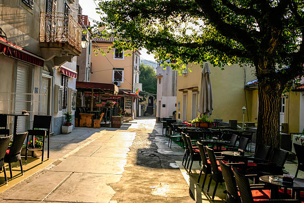 A cozy outdoor cafe: empty wooden tables with flowerpots and menu papers on them; an exterior of an empty street bar in the daytime, pavement-stone on the ground, Lisbon, Portugal