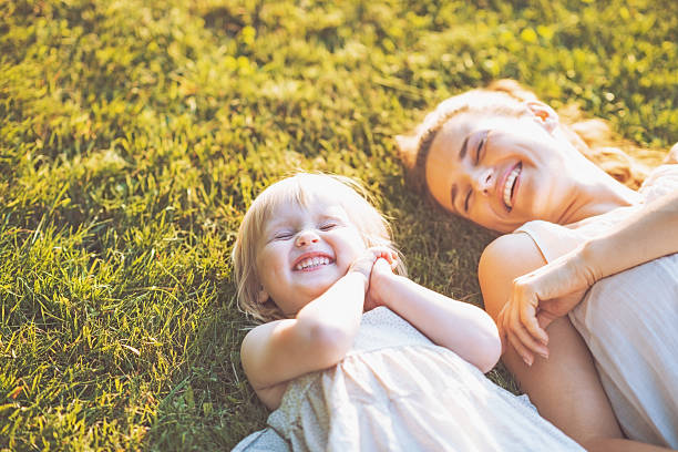 sorridente madre e figlio sdraiati su prato - baby mother summer park foto e immagini stock