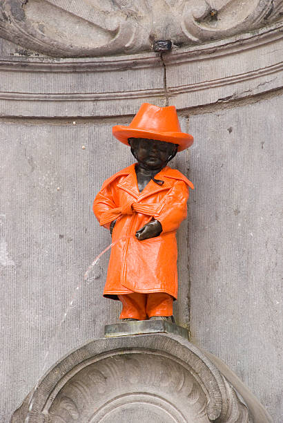 statue Brussels the statue of Manneke Pis, covered with a orange coat manneken pis statue in brussels belgium stock pictures, royalty-free photos & images