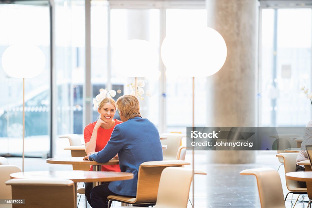 Happy businesswoman looking at colleague in office A photo of happy businesswoman looking at colleague. Business people are sitting at table. Professionals are discussing, in a modern office lobby. Brightly Lit Stock Photo