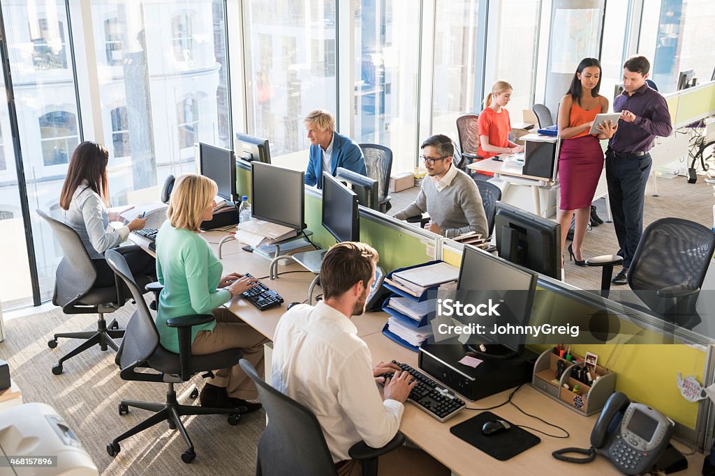 Multi-ethnic business people working together in office A photo of multi-ethnic business people working together. Professionals are using computers and discussing. Desks are located near windows, in brightly lit modern office. 20-24 Years Stock Photo