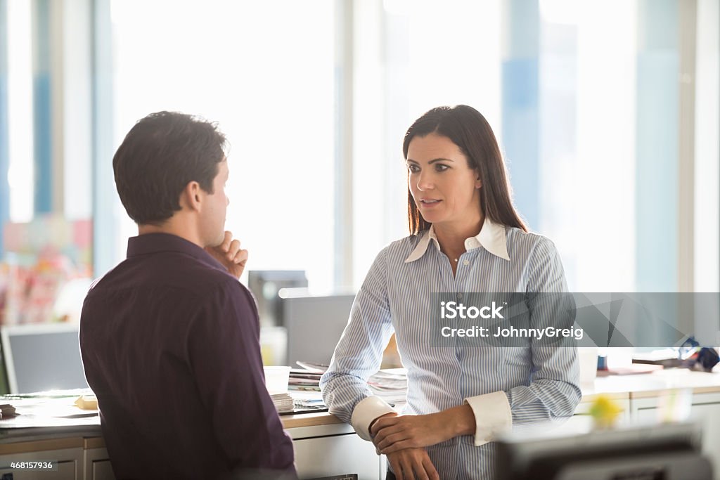 Serious business people discussing in office A photo of serious businesswoman discussing with colleague. Professionals are in formals. Executives are looking at each other, in a brightly lit modern office. 2015 Stock Photo