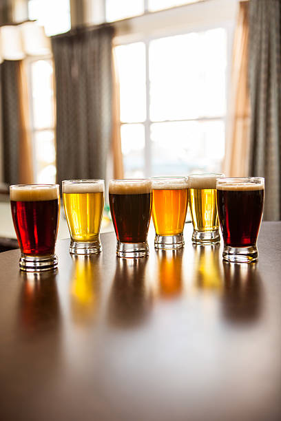 Six tasters of beer set up on a bar.