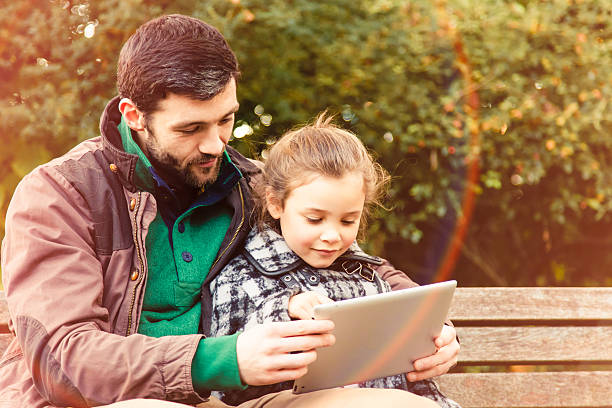 Father and Daughter on a park bench with tablet