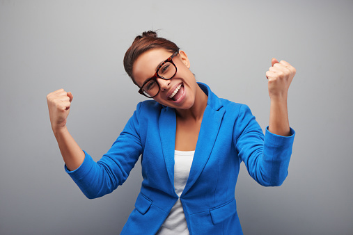 Young mixed race woman with glasses gains a victory, standing on grey background