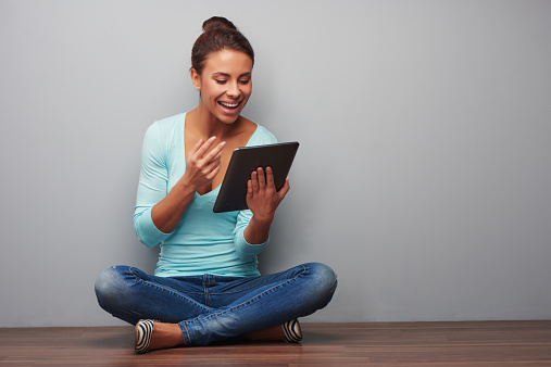 Cheerful mixed race woman working on tablet computer, sitting against grey background