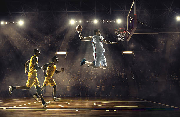 Basketball game Low angle view of a professional basketball game. A player is in mid air holding ball about to score a slam dunk, but the player from the opposite team is ready to block him.  A  game is in a indoor floodlit basketball arena. All players are wearing generic unbranded basketball uniform. basketball player photos stock pictures, royalty-free photos & images