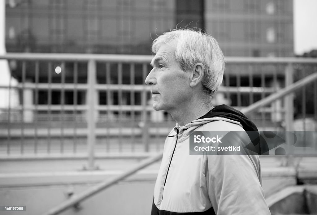 Senior man running. Portrait of senior man wearing sport clothes doing his sport routine at city street.  Urban scene, office building in background. Cold weather, late autumn. Ambient light is used to make this photo, so there is higher amount of noise and some motion blur visible. 2015 Stock Photo