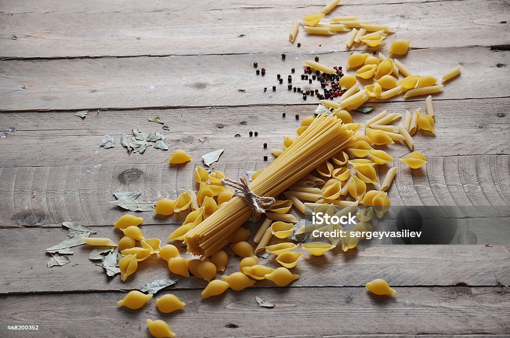 Cooking concept. Uncooked italian pasta Cooking concept. Uncooked italian pasta: vermicelli, spaghetti with twine and tomato on wooden background 2015 Stock Photo