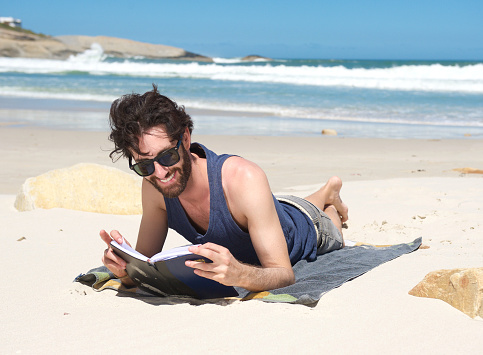 Portrait of a happy young man reading book at the beach