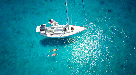 aerial view of honeymoon couple holding hands and snorkeling next to a luxury sailboat moored in the Caribbean