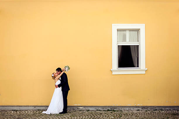 Newlyweds kissing Newlyweds kissing in front of a yellow wall with window. About 25-30 years old, Caucasian couple in wedding dress and suit. wedding dress photos stock pictures, royalty-free photos & images