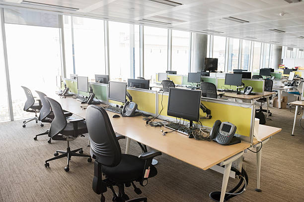 Modern brightly lit office with empty workstations A photo of empty workplace. Computers and chairs are arranged at desks. They are located near windows, in a brightly lit contemporary office. office cubicle no people stock pictures, royalty-free photos & images
