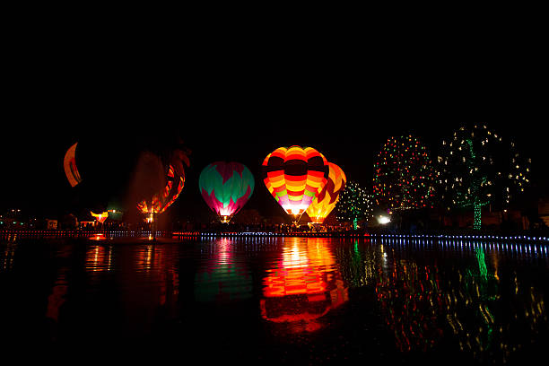 Night Hot Air Balloon Lighting Evening hot air balloon lighting over a lake with Christmas/holiday lights decorating trees in the foreground. Night balloon firing entertains visitors during an Arizona balloon festival. Balloon reflections glow in the lake. ballooning festival stock pictures, royalty-free photos & images