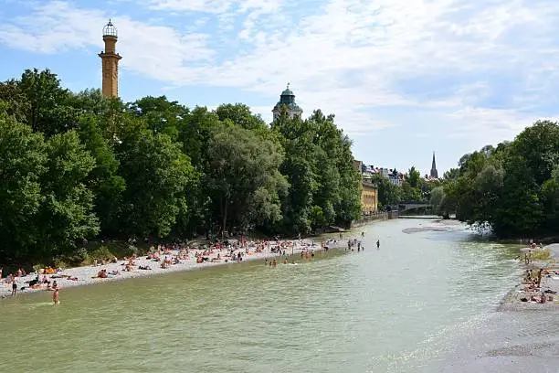 Isar beach in Munich. Locals and tourists spreading their towels for sunbathing on the gravel beach and refreshing in the cold river water on hot summer day. 