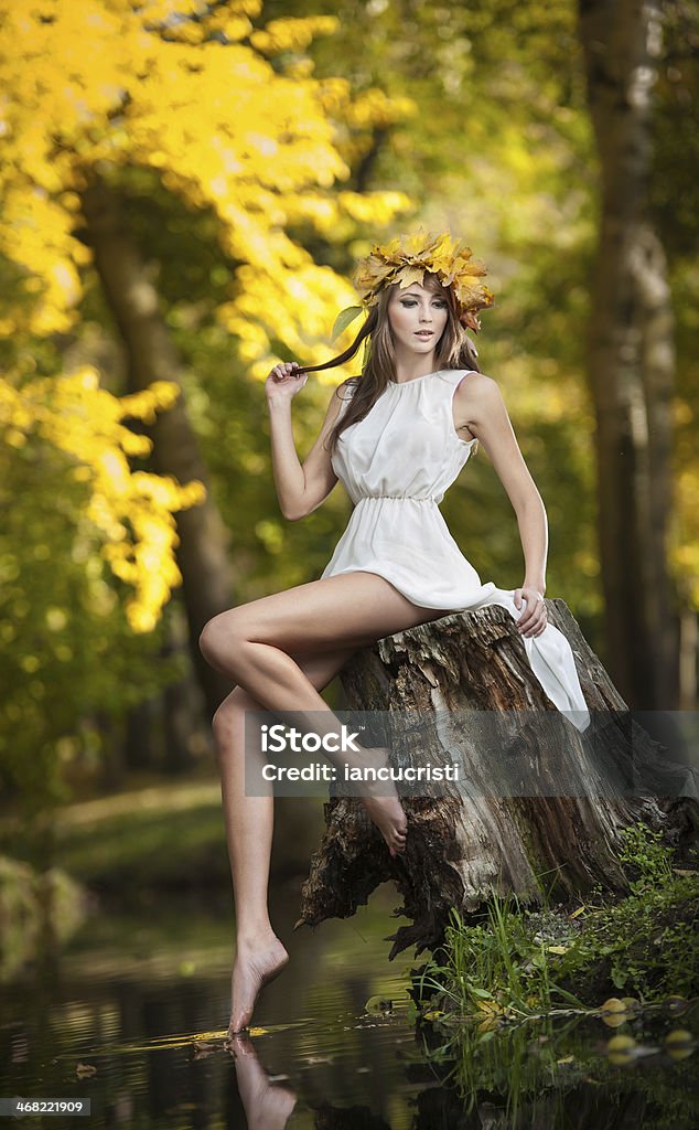 Girl with fairy look in autumnal shot Portrait of beautiful lady in the forest. Girl with fairy look in autumnal shoot. Girl with Autumnal Make up and Hair style. Romantic women with short white dress posing in autumnal park Adult Stock Photo