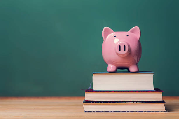 Piggy bank on top of books, cost of education theme Pink Piggy bank on top of books with chalkboard in the background as concept image of the costs of education financial education stock pictures, royalty-free photos & images