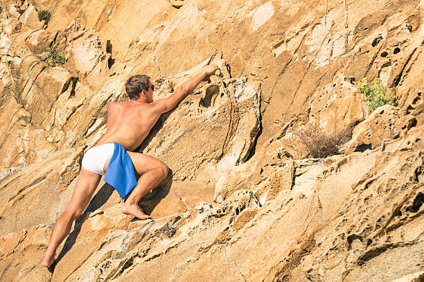 Young athletic man free climbing without equipment on dangerous rock slope - Adventurous concept of freedom and contact with wild nature