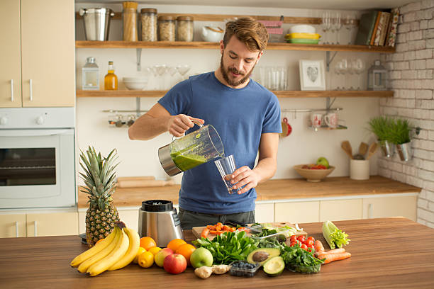 young man making juice or smoothie in kitchen. - 榨汁機 個照片及圖片檔