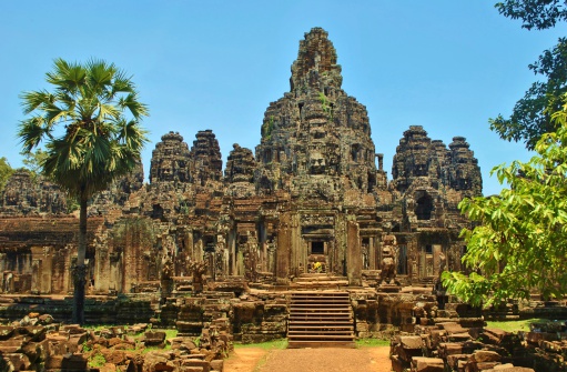 The Bayon (Angkor Thom) Khmer temple surrounded by palm trees and greenery in the sunshine at Angkor, Siem Reap, Cambodia