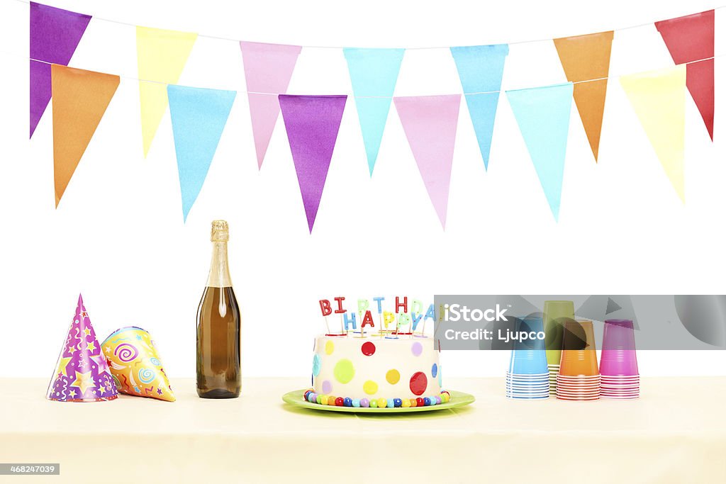 Bottle of champagne plastic glasses, party hats and birthday cake Bottle of sparkling wine, plastic glasses, party hats and birthday cake isolated on white background Table Stock Photo