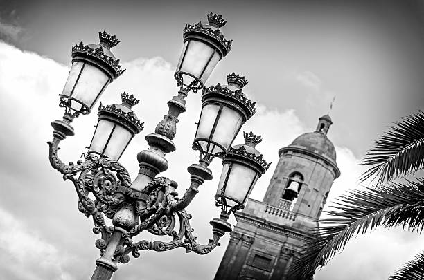 A black and white shot of the cathedral of Las Palmas.  In the front of the image you can see the beautiful ornate street lamps found outside this incredible building.
