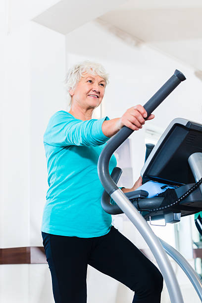 femme âgée sur appareil elliptique de l'exercice dans la salle de sport - cross trainer photos et images de collection