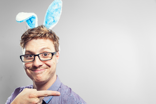 An Easter nerd with blue rabbit ears pointing to the right of shot, wearing a purple business shirt, tie and glasses. THere's plenty of space for your Easter message.