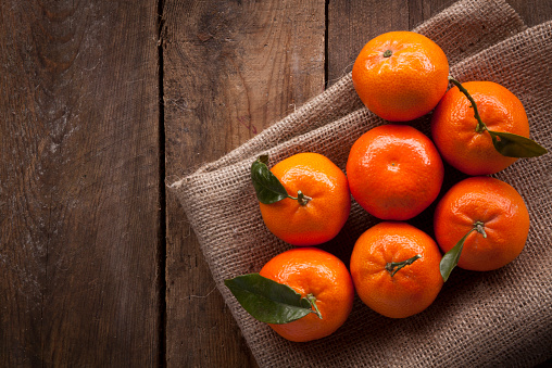 A tumble of fresh mandarins shot overhead on rustic worn wood and hessian cloth, lit by natural daylight. 