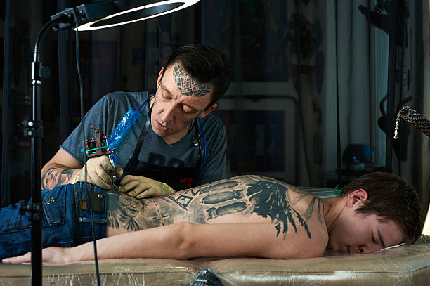 Tattooist makes a tattoo on the back Tattooist makes a tattoo on the back of a guy shoulder tattoo designs for men stock pictures, royalty-free photos & images