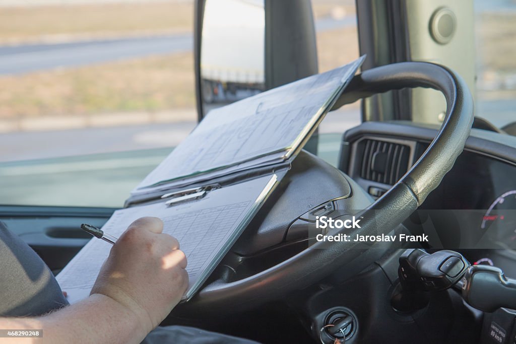 Truck driver is writing in the documentation. Closeup view of the hands of truck driver who is is writing in the documentation driver. Photo shooted in the vehicle cabin. Document Stock Photo