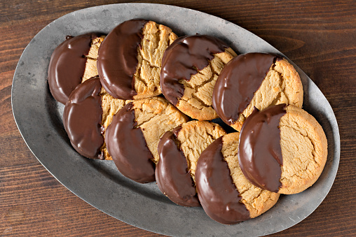 An overhead, extreme close up, horizontal photograph of a gray pewter platter with some chocolate dipped peanut butter cookies.