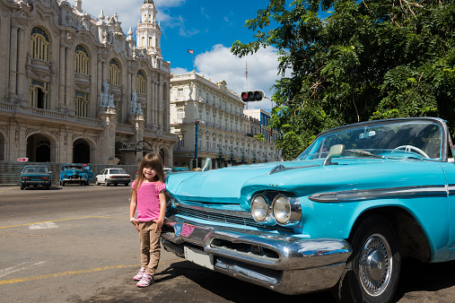 Child enjoying a vacation in Cuba next to a classic car in Havana