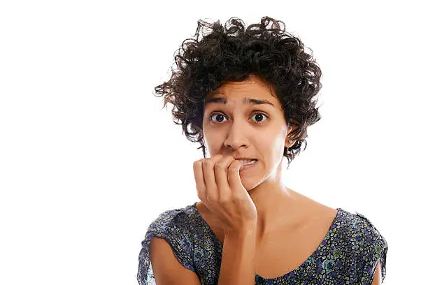 portrait of worried and stressed hispanic girl biting nails and looking at camera on white background