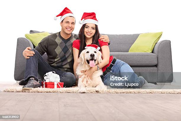 Young Couple With Santa Hats Sitting With A Dog Stock Photo - Download Image Now - 20-29 Years, 2015, Adult
