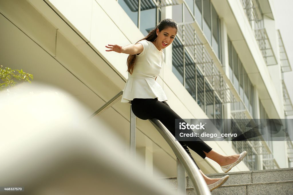 Cheerful Business Woman Going Downstairs Sliding On Rail For Joy Happy hispanic businesswoman, girl, latina woman, successful fermale manager sliding on rail. Joy, happiness for business success and career Sliding Stock Photo