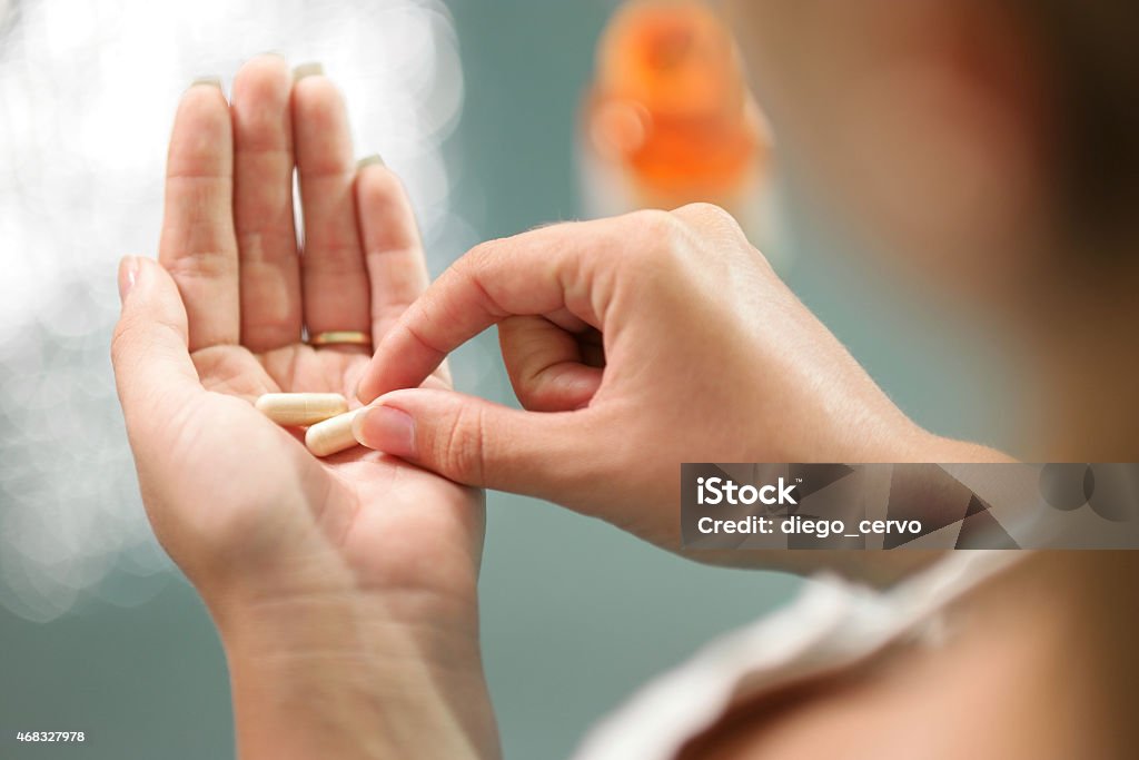 Young woman taking vitamins ginseng pill Close up view of young woman holding ginseng vitamins and minerals pills in hand with capsule bottle on table. High angle view Capsule - Medicine Stock Photo