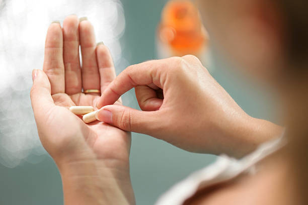 Young woman taking vitamins ginseng pill Close up view of young woman holding ginseng vitamins and minerals pills in hand with capsule bottle on table. High angle view pill photos stock pictures, royalty-free photos & images